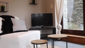 Une chambre moderne avec un lit, une télévision, deux petites tables et un mur en pierre apparent.