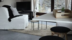 Un salon moderne avec un canapé blanc, un téléviseur, une table basse en bois et deux tabourets noirs.