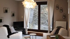 Un salon moderne avec un canapé, un téléviseur et une grande fenêtre agrémentée de rideaux.