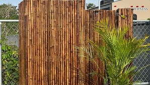 Valla de bambú en un jardín con planta en maceta y un banco de madera pequeño.
