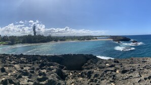 Paisaje costero con playa, primer plano rocoso y cielo despejado.