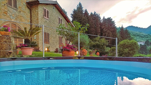 A clear swimming pool with a stone building in the background, surrounded by potted plants and trees. - VILLA CAMELIA TUSCANY villa with pool surrounded by olive trees - wonderful view (Pescia)