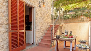 A stone building with a wooden door and shutters, a staircase, and a table with a bottle and fruits. - VILLA CAMELIA TUSCANY villa with pool surrounded by olive trees - wonderful view (Pescia)