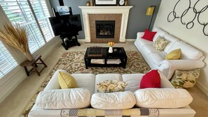 A living room with a white sofa, a chessboard, a fireplace, and a TV. - Fully furnished elegant suburban house with desirable amenities and location. (Calgary)