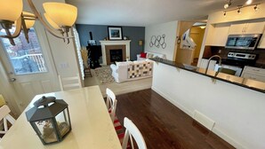 A modern kitchen with white cabinets, a microwave, and a stove. There is a dining area with a table and chairs, and a fireplace in the background. - Fully furnished elegant suburban house with desirable amenities and location. (Calgary)