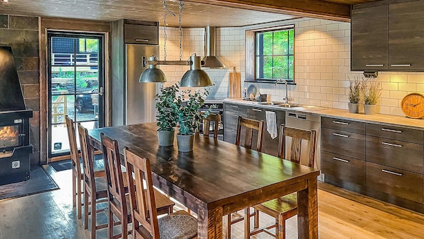 A modern kitchen with a large wooden table, dark cabinets, and a built-in stove.