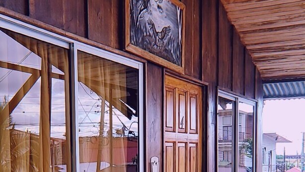 A wooden bench in a covered outdoor area with large windows and a door. - Alpha Arenal - Hostel (La Fortuna)