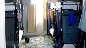 A narrow corridor with bunk beds on either side, a tiled floor, and a single light source at the end. - Alpha Arenal - Hostel (La Fortuna)