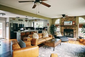 A spacious living area with a leather sofa, a coffee table, and a fireplace. - Luxe Catskills Cabin | Hot Tub, Fire Pit, Fishing (Cairo)