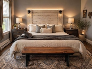 A bedroom with a large bed, bedside tables, a bench, and a wall-mounted lamp.