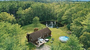Uma cabana com varanda e piscina, rodeada por floresta densa e montanhas.