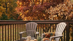Een houten terras met twee Adirondack stoelen, een klein tafeltje met een mok en muffins, en een geruite plaid.'