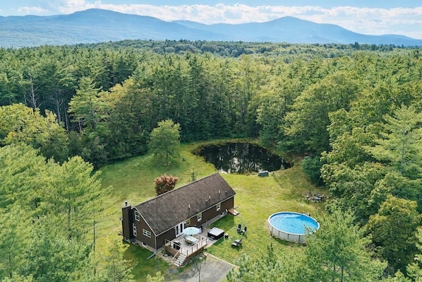A house surrounded by a dense forest with a swimming pool in the backyard.
