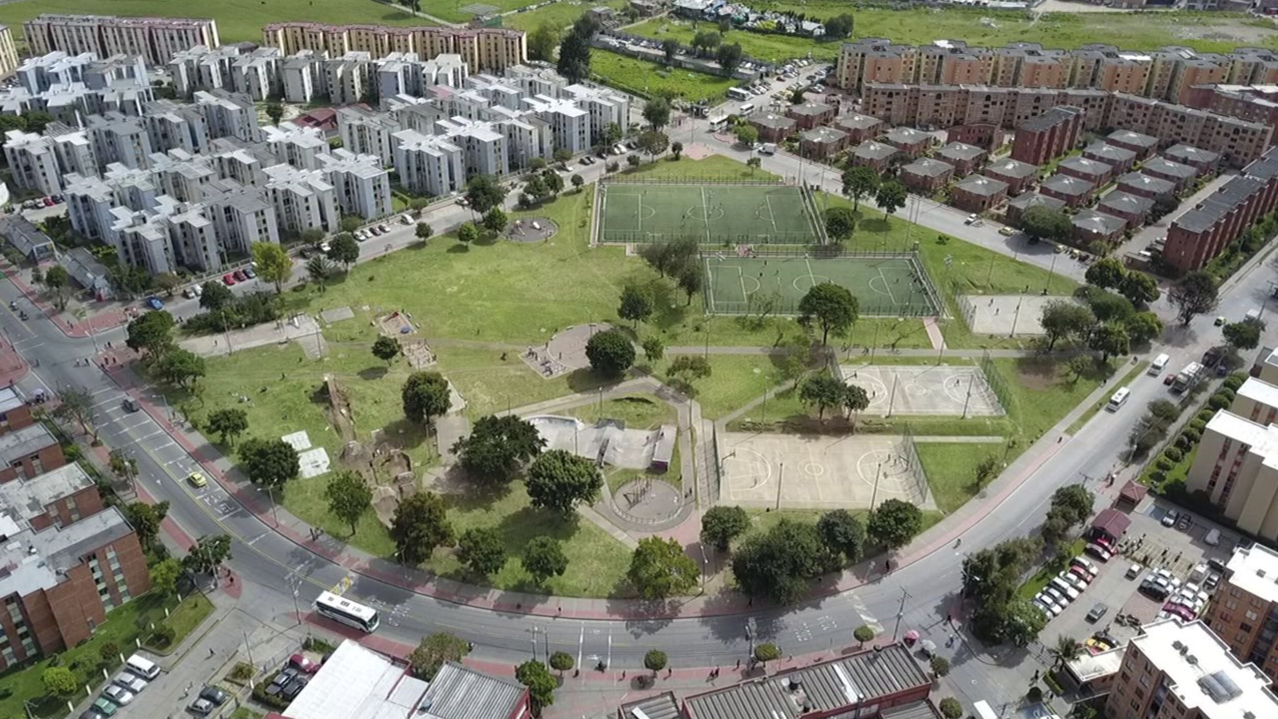 Vista aérea de una zona residencial con varios edificios de apartamentos, un espacio abierto central con cancha de baloncesto y carreteras circundantes.