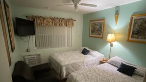 A room with two beds, a ceiling fan, a TV, a lamp, and a framed picture on the wall.