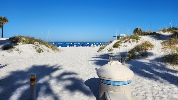 A sandy beach path leading to a beach area with blue umbrellas and a small structure.