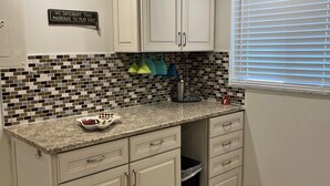 A kitchen with white cabinets, a tiled backsplash, and a window with blinds.