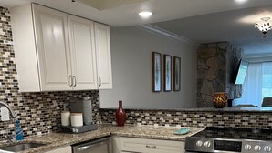 A modern kitchen with white cabinets, a granite countertop, a built-in oven, and a stone backsplash.