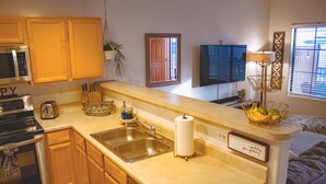 Una cocina con armarios de madera, un microondas de acero inoxidable, un fregadero y una encimera con una cesta de fruta y una lámpara.