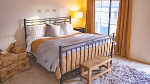 Una cama bien hecha con cabecera de madera, una lámpara de noche y un banco.