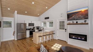 A modern kitchen with a central island, a fireplace, and a large TV on the wall.