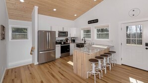 A modern kitchen with a central island, stainless steel appliances, and a wooden ceiling.