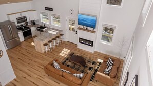 A modern kitchen with a central island, a dining area with bar stools, a cozy seating area with a sofa and a coffee table, and a fireplace.
