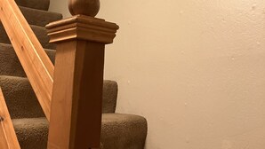 Una escalera con balaustres de madera y barandilla, que conduce a una plataforma con dos cuadros enmarcados en la pared.