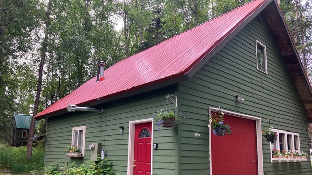Una casa de madera verde con puerta roja y garaje, rodeada de follaje.