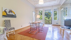 A spacious living room with a dining area, a large window with a view of trees, and a television on a wooden table. - 4 bedroom stunning apartment in Genova (Genova)