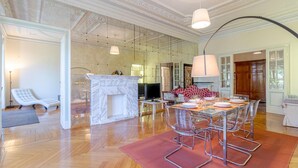 A spacious living room with a fireplace, a dining area with clear chairs, and a modern kitchen visible through glass walls. - 4 bedroom stunning apartment in Genova (Genova)