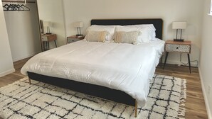 Um quarto bem arrumado com uma cama grande, duas mesas de cabeceira com abajures, um guarda-roupa e um tapete estampado.