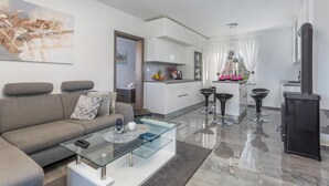 A modern living room with a glass coffee table, a grey sofa, and a kitchen area with a dining set.