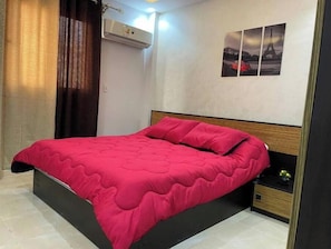 A bedroom with a bed, a nightstand, an air conditioning unit, and wall art. - 3 bedrooms Family apartment (محاف ظة القاهرة‬)