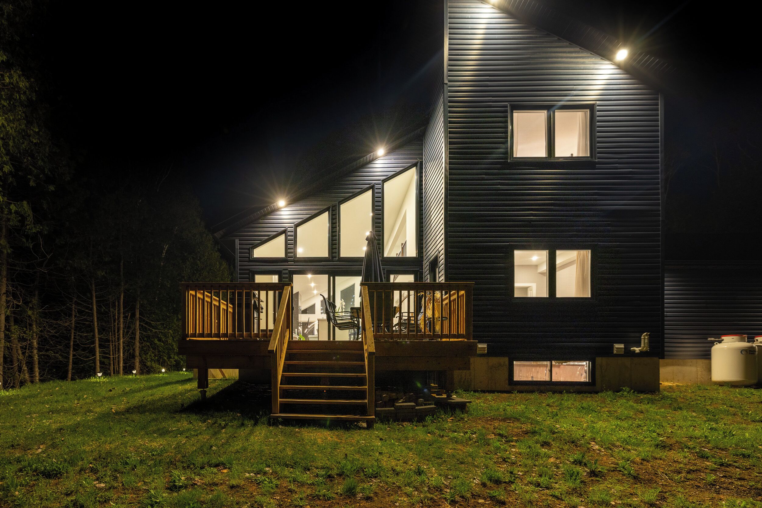 Una casa moderna con terraza de madera y una escalera que lleva a una puerta de cristal.