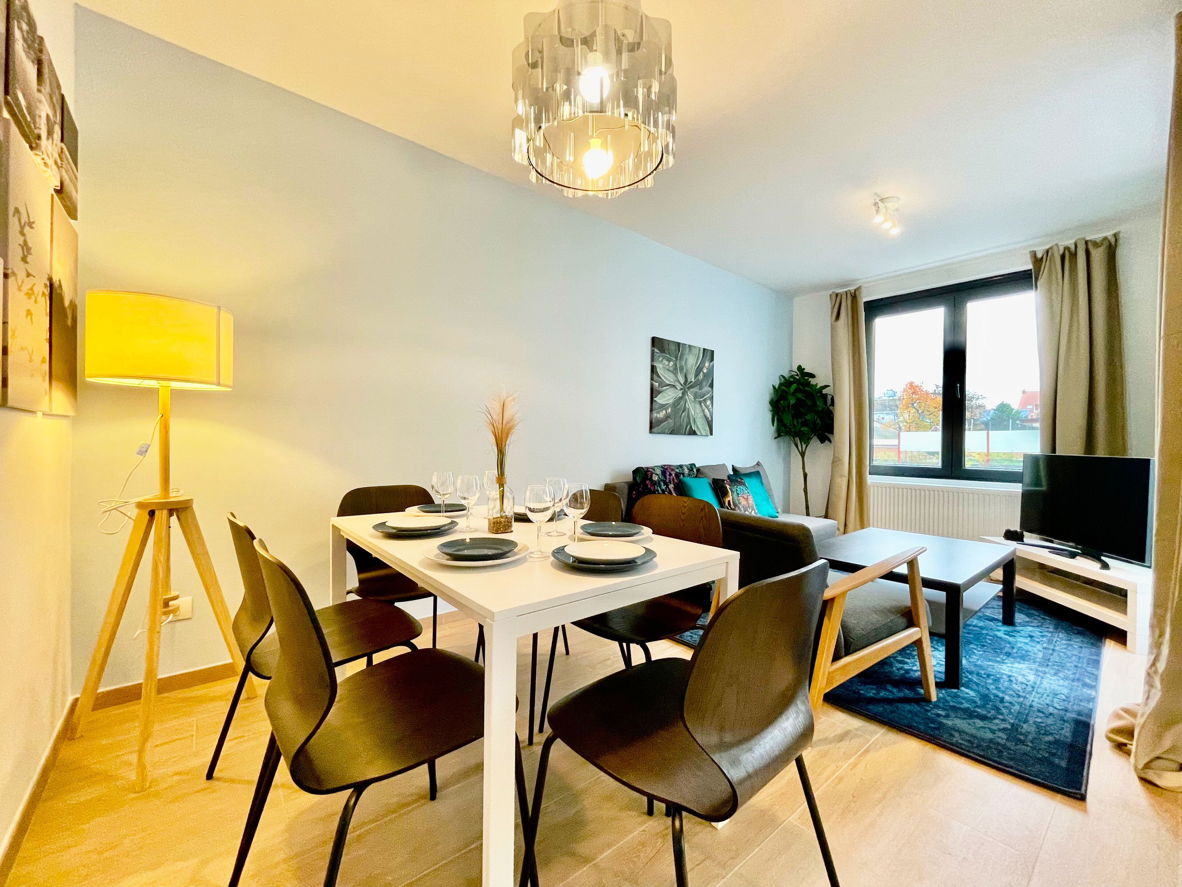 A modern living room with a dining area, a large window, a flat-screen TV, and a floor lamp.