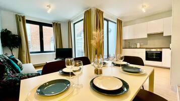 Comedor con una mesa lista para cuatro personas, un televisor y vistas de la ciudad a través de amplios ventanales.