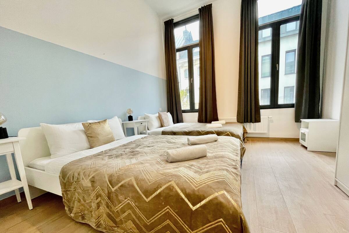 Ein Hotelzimmer mit zwei Betten, einem weißen Sofa, einem kleinen Tisch und einem Fenster mit Vorhängen.