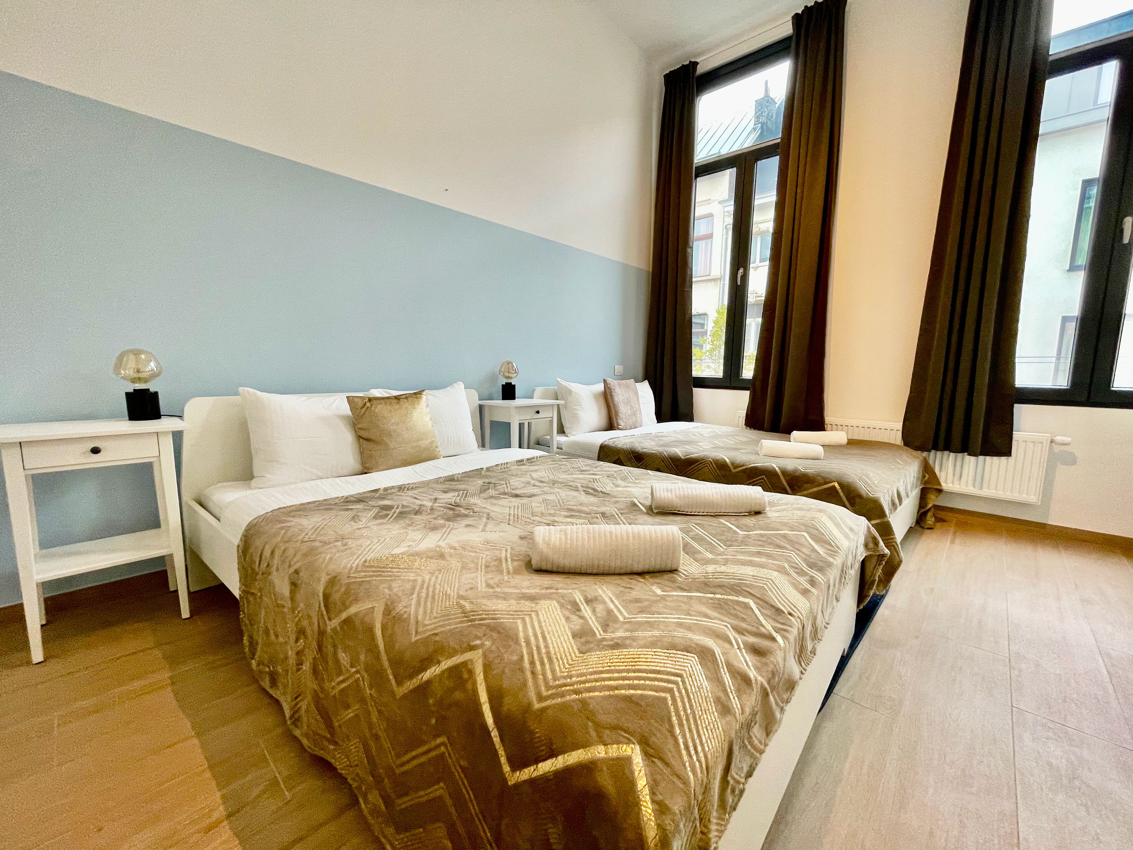 Une chambre d’hôtel avec deux lits, une table de chevet, une lampe et une fenêtre avec des rideaux.