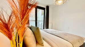 A bedroom with a bed, pillows, a vase with dried plants, and a window with a view of a balcony. -  One Lux Stay near Fashion District (Antwerp)