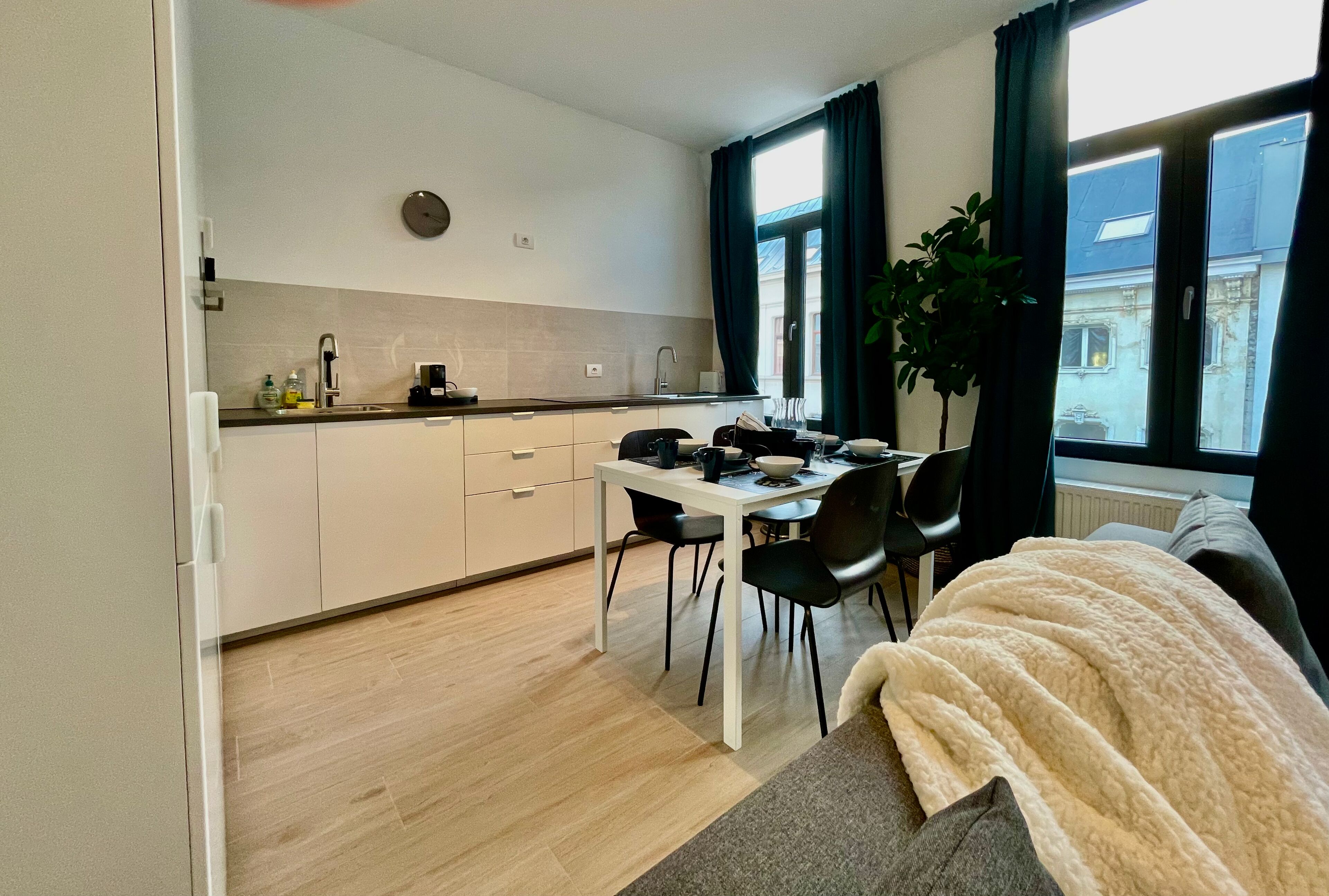 Eine kleine Küche mit Essbereich, ein großes Fenster mit Vorhängen und Blick auf Gebäude.