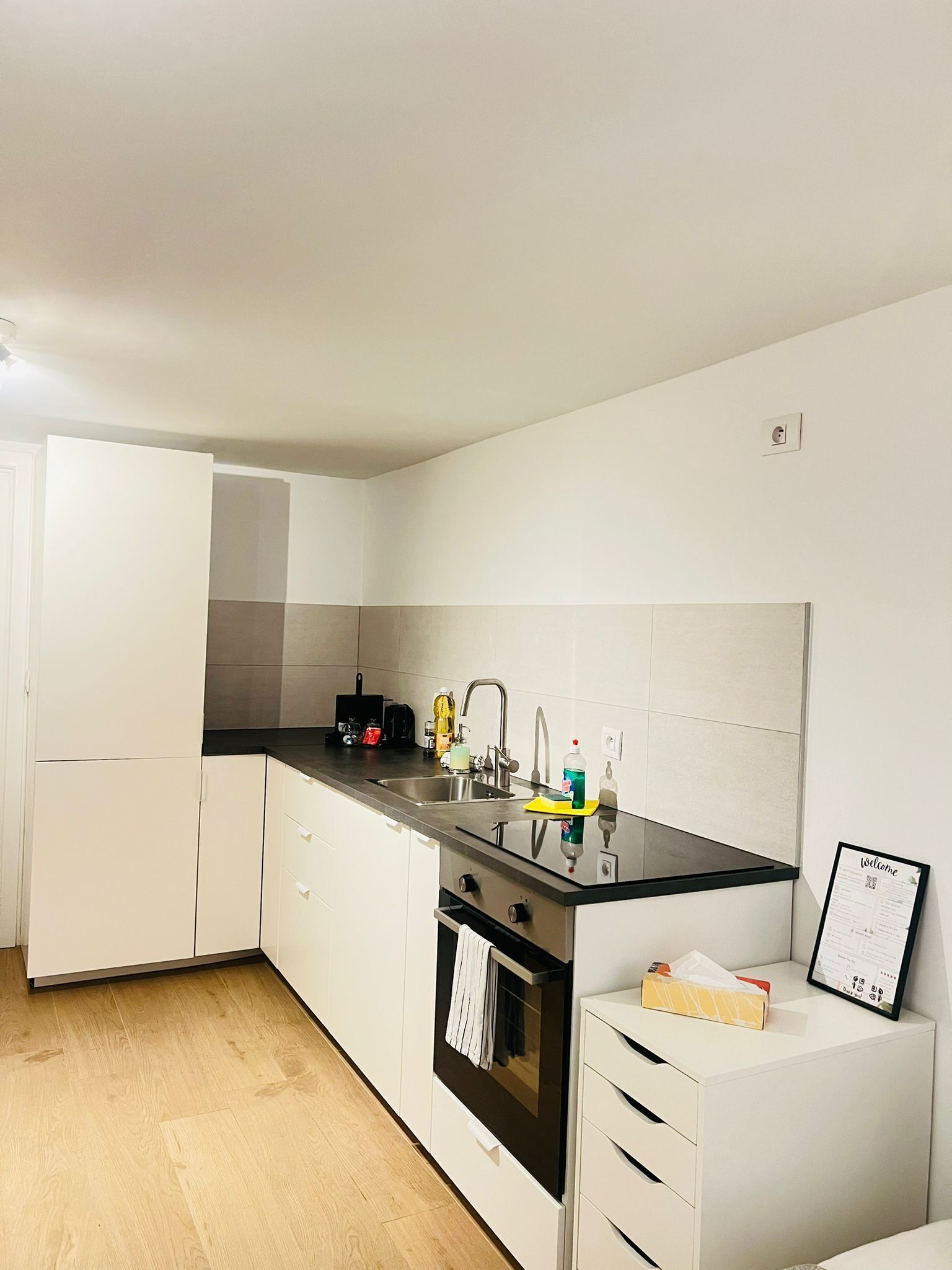 A modern kitchen with white cabinets, a black countertop, stainless steel sink, and an oven.