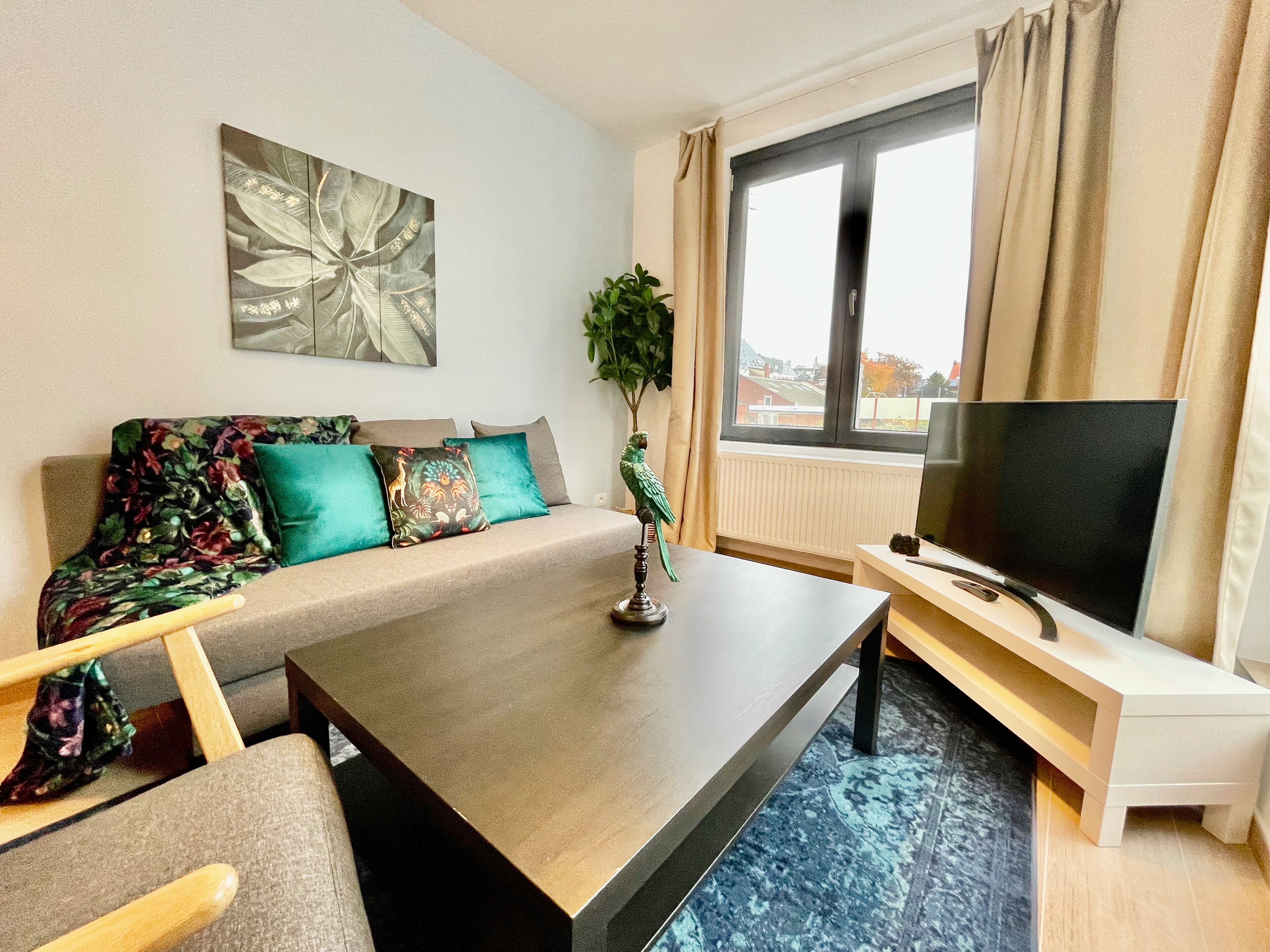 Een moderne woonkamer met een bank, salontafel, televisie en een groot raam met gordijnen.