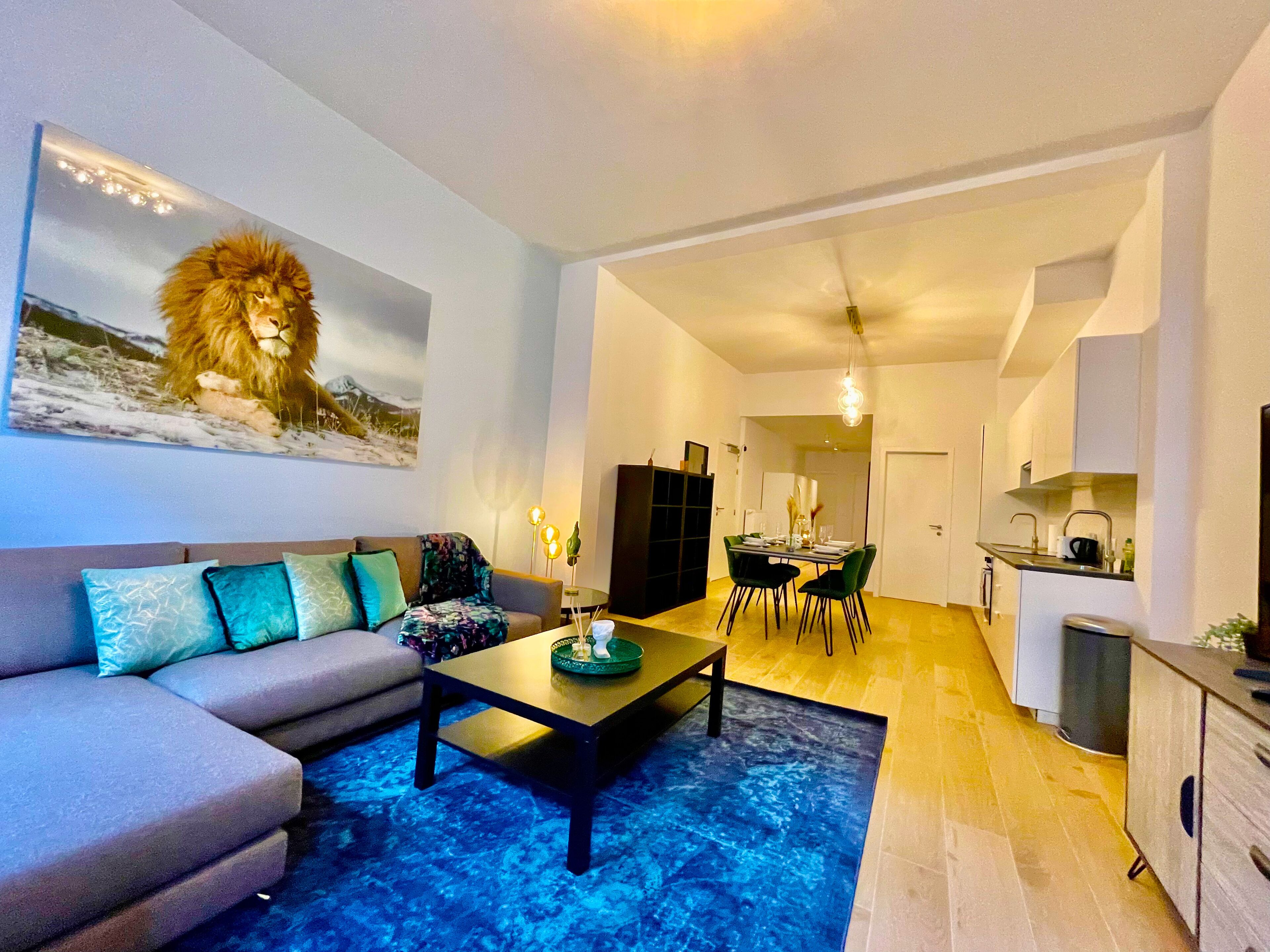 Ein modernes Wohnzimmer mit einer Couch, einem Couchtisch und einem Gemälde eines Löwen. Es gibt einen Essbereich mit Stühlen und einem Tisch.
