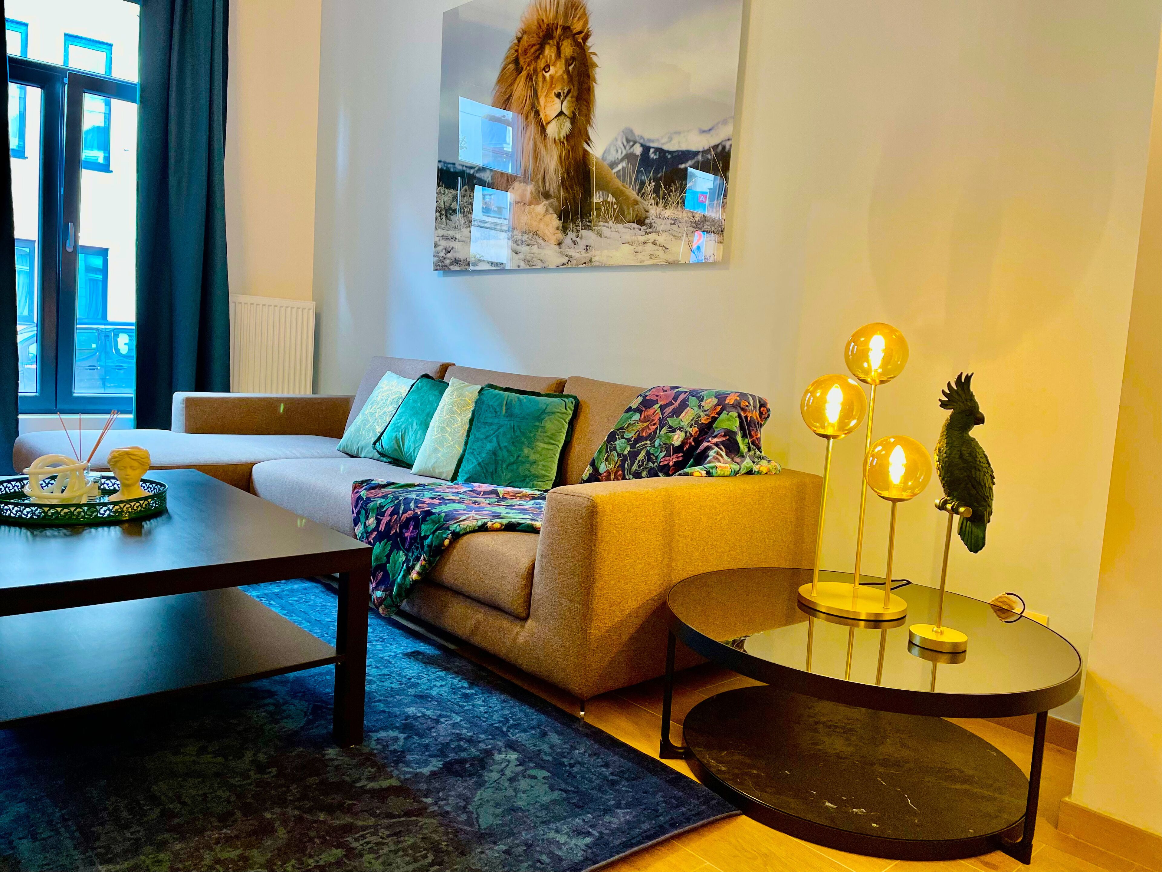 Un soggiorno moderno con un divano, un tavolino da caffè, un tavolo con piano in vetro e luci decorative, e un quadro appeso al muro raffigurante un leone.
