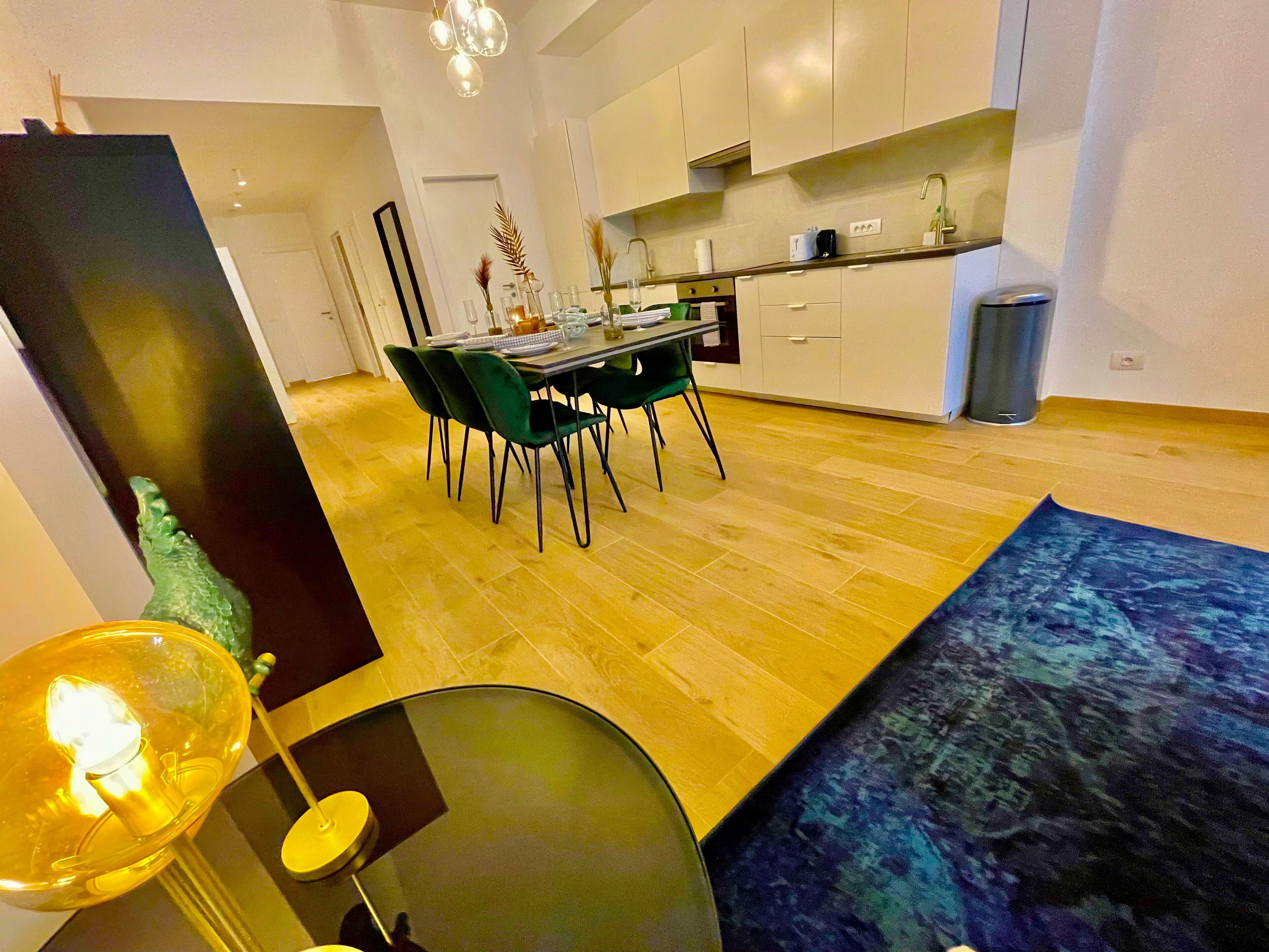 A modern kitchen with white cabinets, a dining area with green chairs, and a small table set for two.