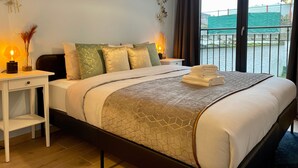 A neatly made bed with a geometric patterned blanket, a bedside table with a lamp, and a view of a balcony with a railing. -  One Lux Stay near Fashion District (Antwerp)