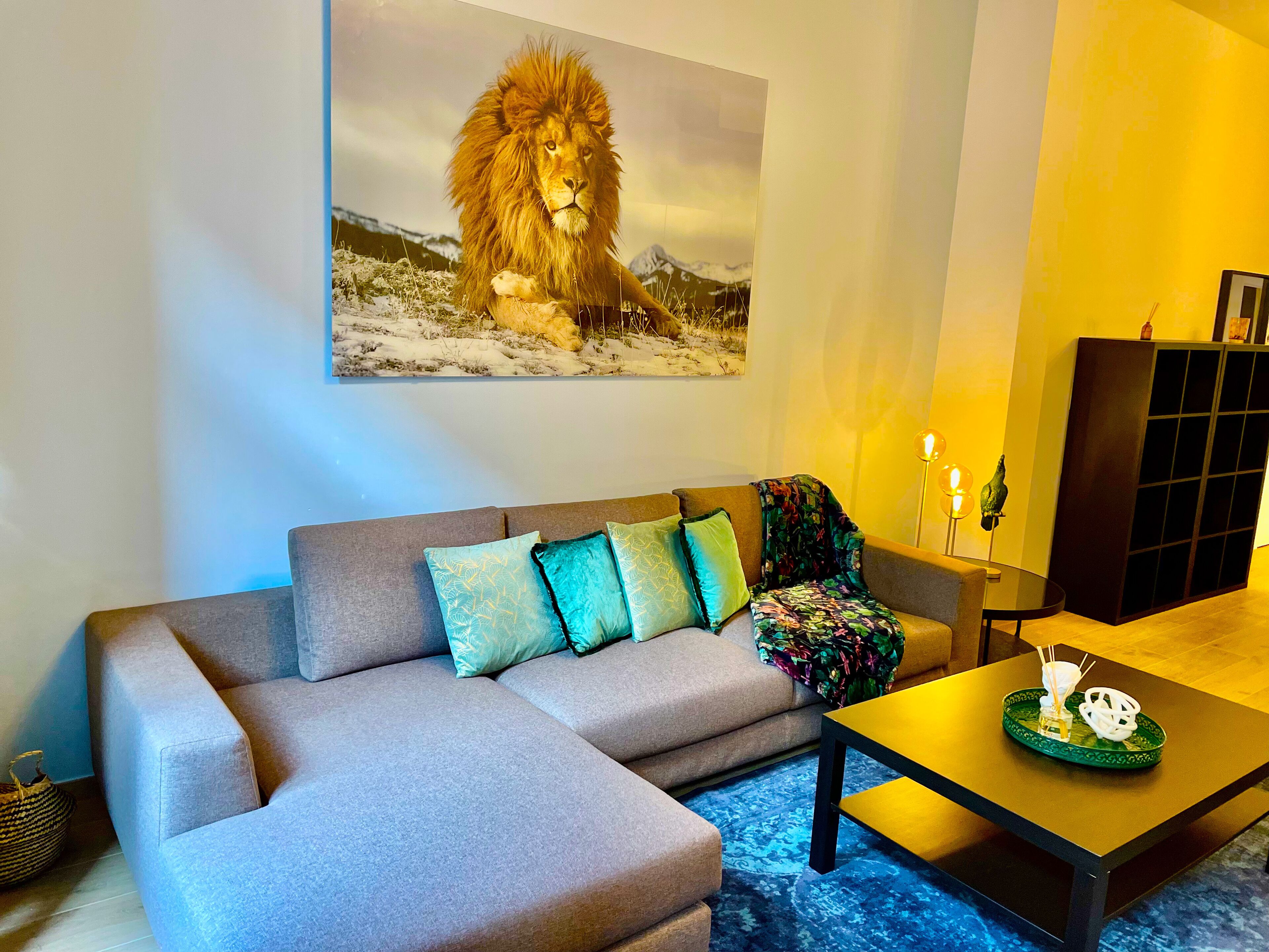 Een woonkamer met een grijze hoekbank, een salontafel, een schilderij van een leeuw en een kast.