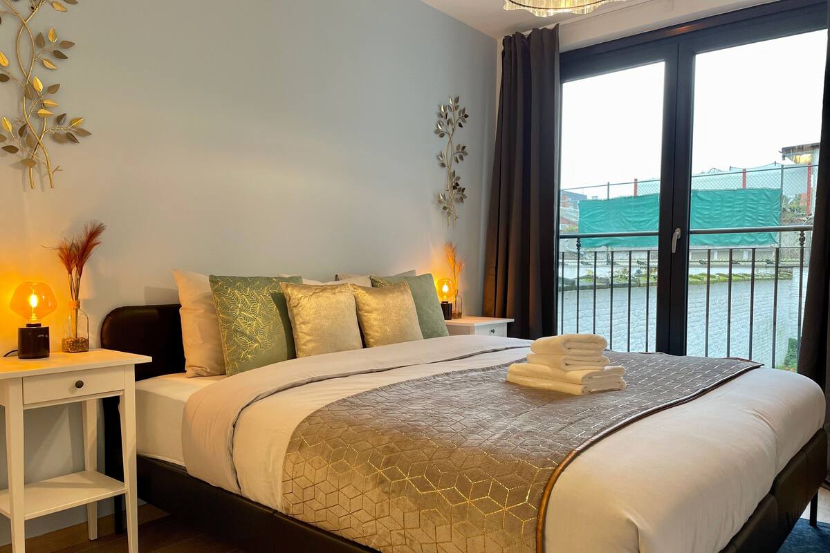 Ein Hotelzimmer mit Bett, Nachttischen, Blick auf ein Gewässer und einem Balkon.