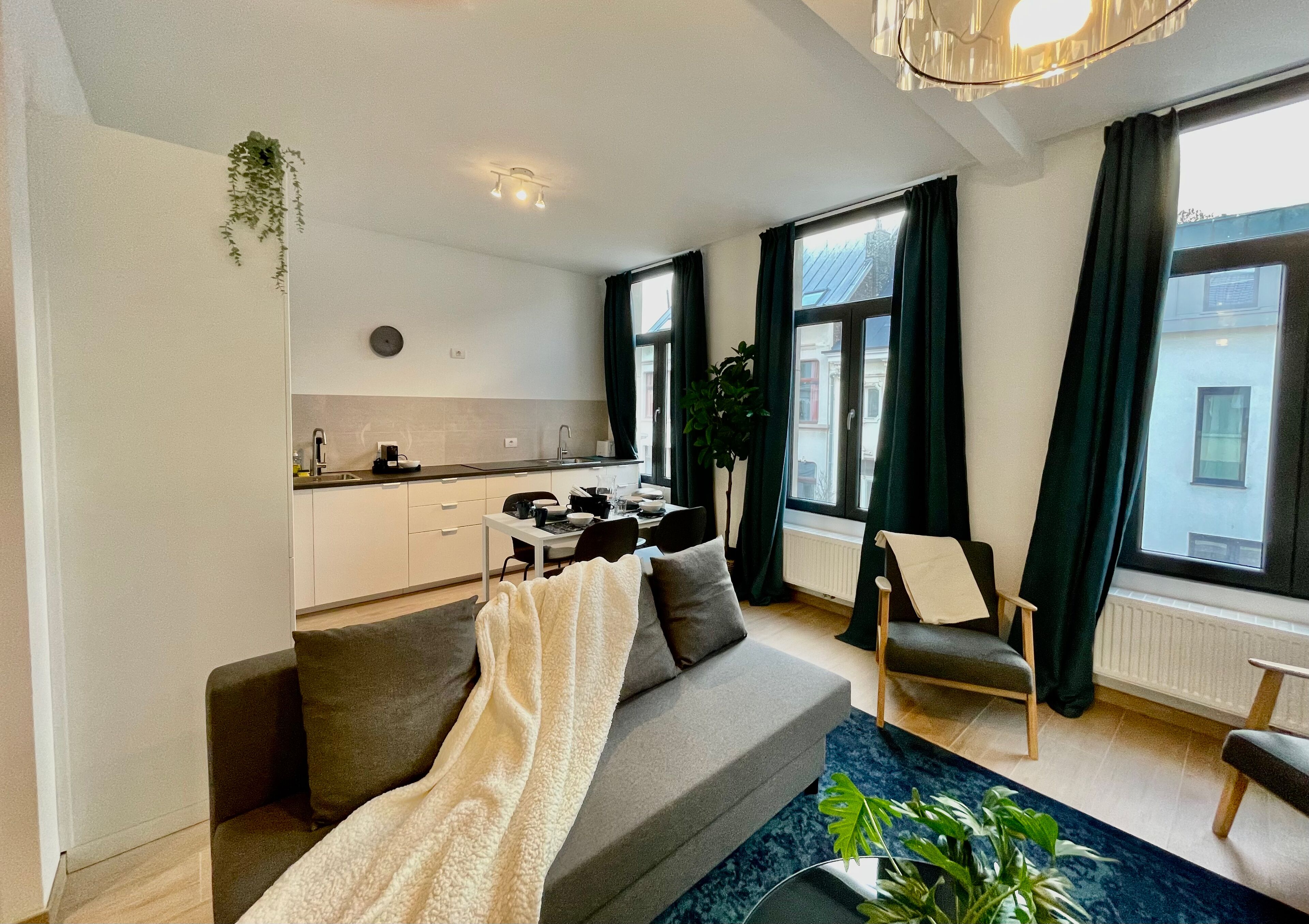 Un salon moderne avec un canapé gris, une table basse et, au fond, un coin repas.